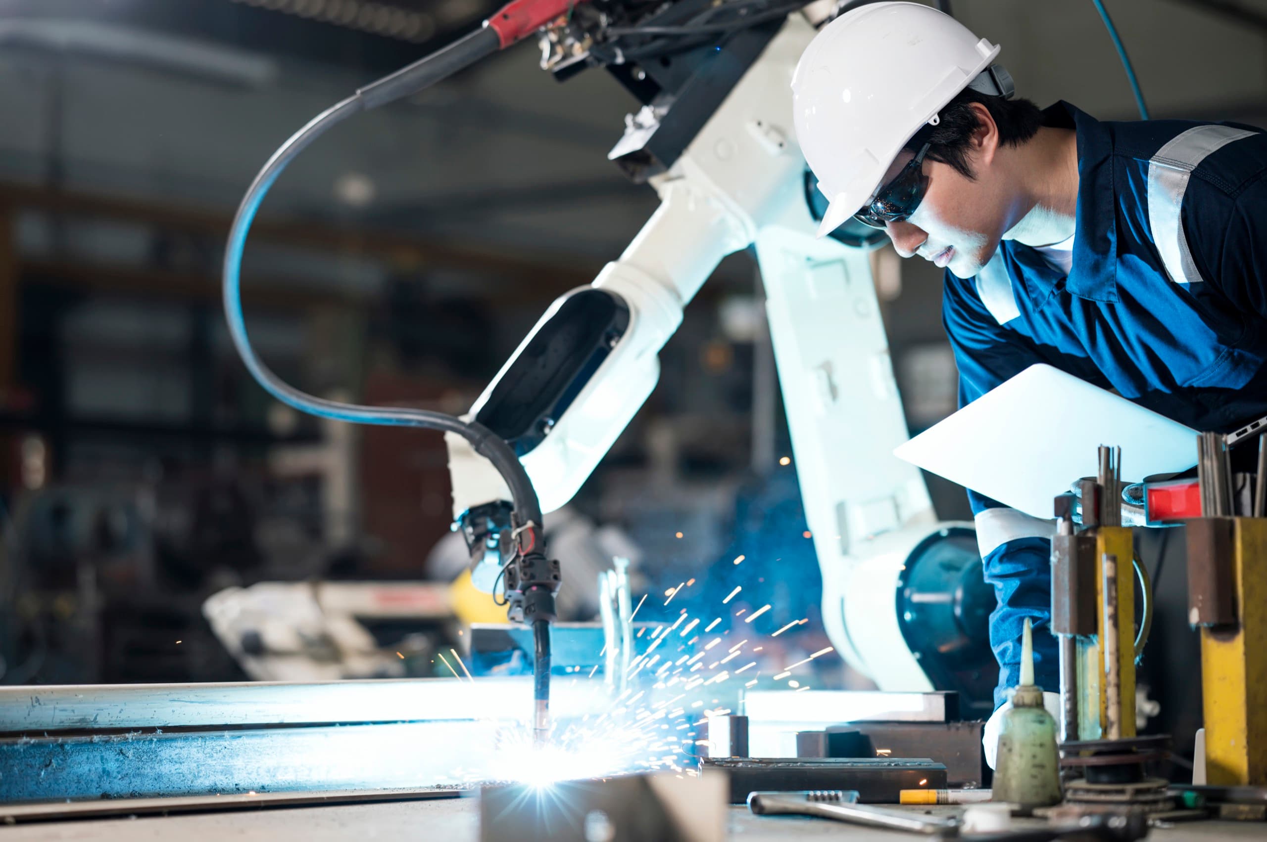 Tekniker övervakar robotsvetsning med gnistregn i metallverkstad